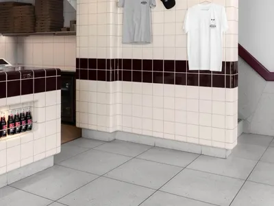 A casual restaurant interior with a tile-covered wall displaying clothing and hats, including two white shirts and three black hats