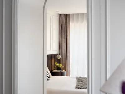 Cozy bedroom with a white bed, black pillows, and ample lighting from two lamps and large windows