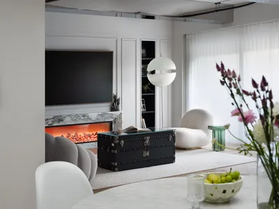 Cozy living space with a fireplace, a couch, chairs, and a dining table, featuring a mix of white and brown tones, with vases and apples adding a touch of freshness