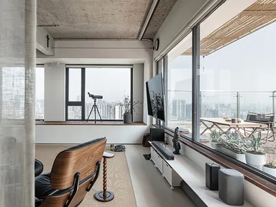 Comfortable living space with a large window, two chairs, a couch, TV, and a potted plant, well-lit by natural sunlight
