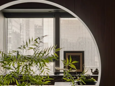 A bright and inviting living area with a large window, potted plants, a vase, chair, and bowl, surrounded by natural light