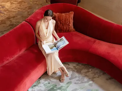 一位女性坐在紅色沙發上，位於寧靜的客廳，地毯鋪地，周圍氛圍平和
