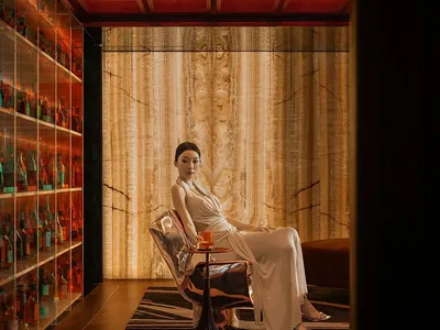 一位女士坐在椅子上，位於裝潢精緻的客廳，旁有酒瓶與酒杯，傳達舒適與精緻的氛圍