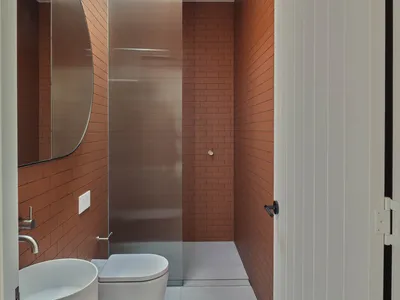 Bathroom with two sinks and a toilet, featuring brown brick walls and a warm atmosphere