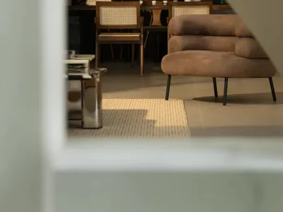 Cozy living space with a brown couch, chairs, and a dining table, lit by natural light from a window