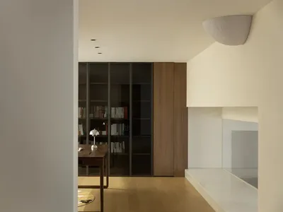 A warm and inviting living space with wooden floors, white walls, bookshelves, a dining table, and a chair, perfect for relaxation and socializing