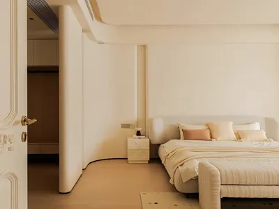 Empty minimalist bedroom with a white bed against a wall, hardwood floor, and white walls
