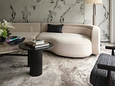 Modern living room with a large couch, marble tiles, a black coffee table, vases, and books, exuding sophistication and comfort