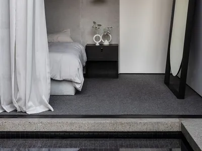 Cozy dimly lit bedroom with a bed in the corner, two vases on the nightstand, and simple furnishings
