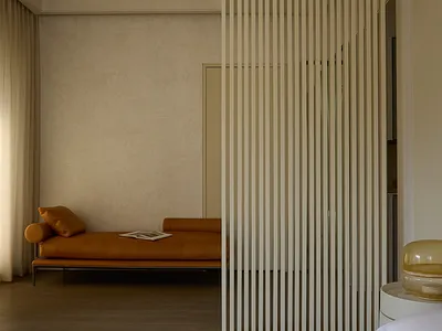 Cozy living room with a couch, two chairs, and a book on the couch, set against a wall with vertical blinds