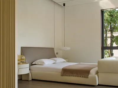 A large bedroom with a minimalist design, featuring a white couch next to a window, two beds, and a chair, giving a calm and inviting atmosphere