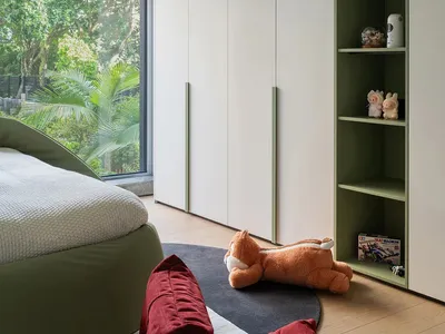 Cozy bedroom with a large bed, a chair, and two teddy bears, featuring a green theme and natural light from the window