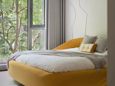 A hotel bedroom with a large yellow bed, white comforter, and orange mattress, featuring two pillows and a window with natural light