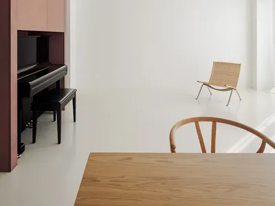 Empty living room with white walls and hardwood floors, featuring a piano, two chairs, and a dining table