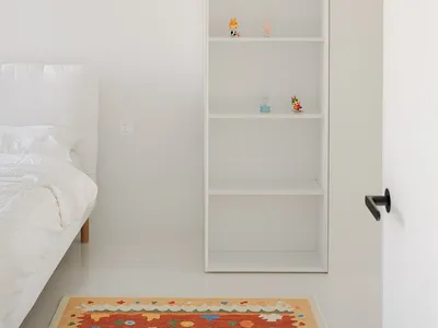 A well-organized bedroom with a large bookshelf filled with books, figurines, and decorative objects, creating an inviting atmosphere
