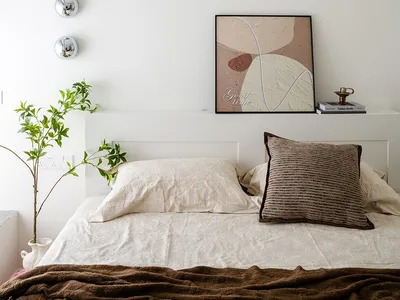 A calm bedroom with a white bed, two potted plants, and a clock on the wall