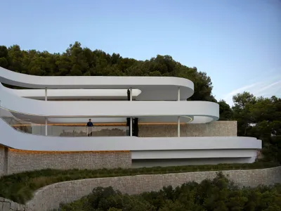 A curved house with a large open area and a spiral staircase in the center, surrounded by stone walls, with natural light illuminating the space