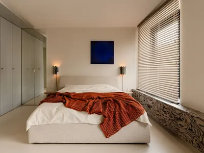 Cozy bedroom with a large white bed, red blanket, and natural light from a window, accompanied by two lamps for additional lighting