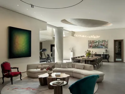 A well-lit living room with a large couch, chairs, dining table, and potted plants, set in a modern home with natural sunlight coming through windows
