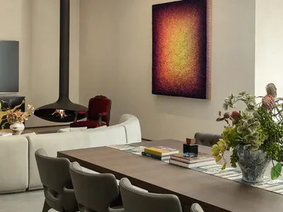 Cozy living space with a dining table, chairs, paintings, and a fireplace, with books and vases adding to the aesthetic