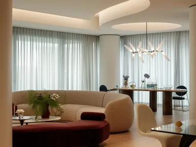A well-lit living room with a modern couch, dining table, chairs, and potted plants, set in a contemporary space with clean lines and minimalistic decoration