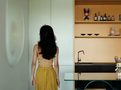 一位女性站在廚房中，有水槽、餐桌和瓶子，周圍配有兩張椅子，營造舒適實用的生活空間