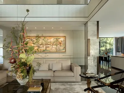 A modern living room with white walls and floors, featuring two couches, a chair, and a vase, with a well-lit and inviting atmosphere