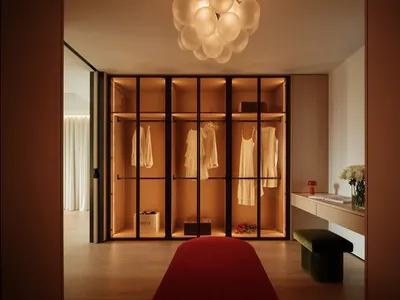 A well-lit bedroom with wooden floors, a red carpet, two wooden closets, a bed, and decorative vases