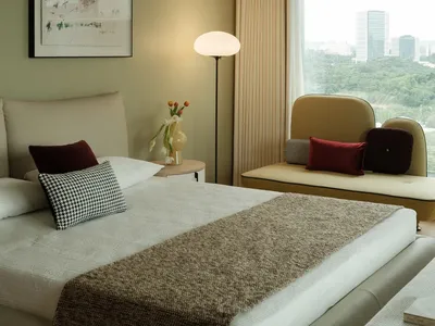 Well-lit bedroom with a large window, two couches, a chair, and a bed, featuring white walls and wooden elements