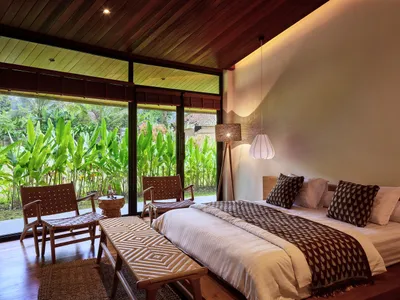 Cozy bedroom with two beds, a wooden floor, and natural light from windows, featuring striped and plain bedding, and two chairs