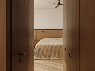 A bedroom with a neatly made bed, wooden doors, and a fan, creating a cozy atmosphere