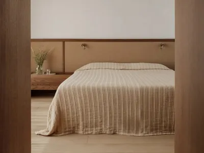 Cozy bedroom with a striped blanket on a hardwood floor, white walls, and a wooden headboard, with two potted plants and a vase nearby