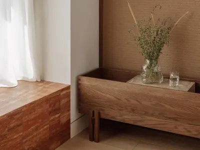A wooden dresser in a well-lit living area with vases and flowers, near a window