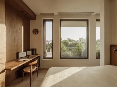 Bright and inviting bedroom with a wooden floor, a chair near the window, clocks, and a book on a surface