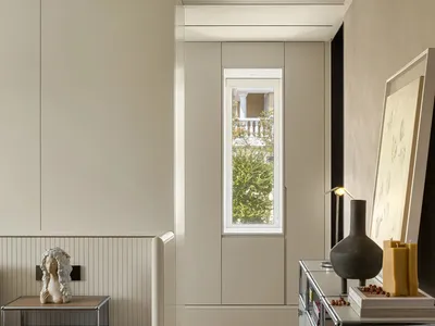 Empty minimalist living room with white walls, a window, and two vases and a book on a table or shelf