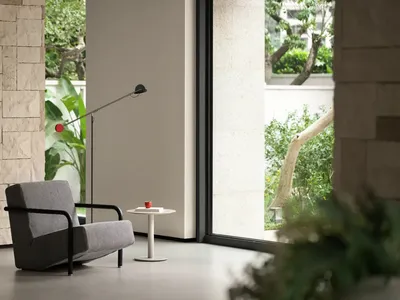 A gray chair sits in front of a window in a calm and inviting living space with natural light and two potted plants nearby