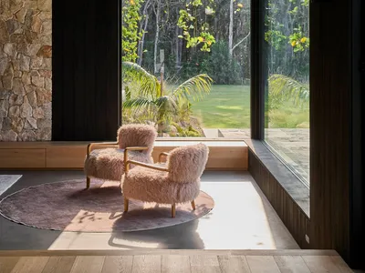 Cozy living space with a black interior design theme, a couch in front of a large window overlooking a garden, and two chairs placed throughout the room
