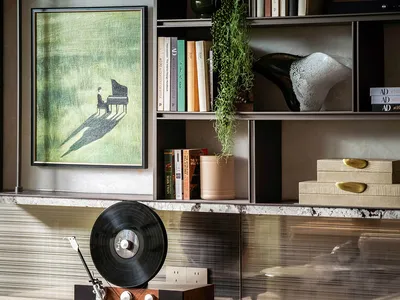 A cozy living room filled with books, a cat statue, and a record player, with a large bookshelf in the background and a vase near the center, reflecting the occupant's interests and personal touches
