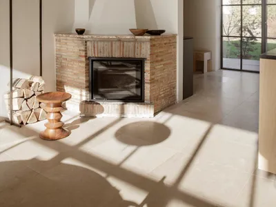Cozy living room with a brick fireplace, a couch, a chair, and a dining table, featuring white walls and warm lighting