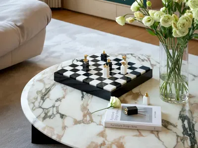 A cozy living room with a black coffee table, chess set, vases of flowers, and scattered books, creating a warm and inviting atmosphere