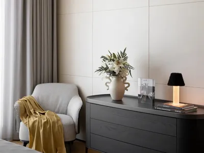 Cozy living room with a couch, two chairs, a table with a vase and book, and a remote control, set against a neutral background