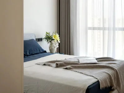 A serene bedroom with a white bed, two vases, and a book, surrounded by natural light from a window