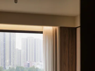 Cozy bedroom with a large window offering a city view, a bed near the window, and two vases on either side