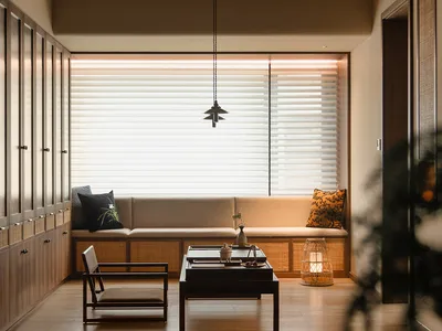 Well-lit living area with a couch, chair, dining table, and potted plants, decorated in neutral tones with a wooden floor