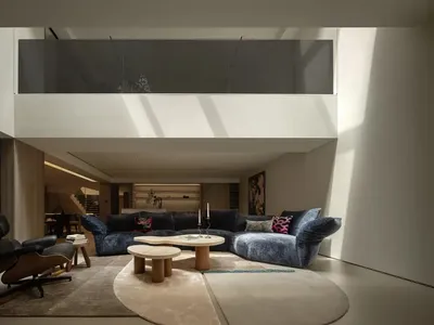 A modern living area with a couch, dining table, chair, and potted plant, well lit with natural sunlight or artificial lighting