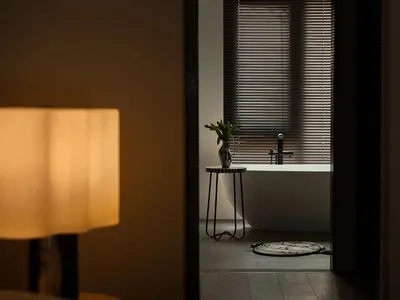 Dimly lit bathroom with a bathtub, black faucet, and vases on a table in front of the tub