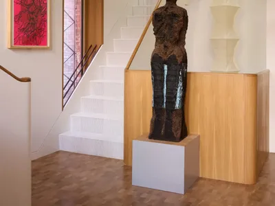 A living area with a wooden sculpture, staircase, and paintings, creating a cozy and unique atmosphere