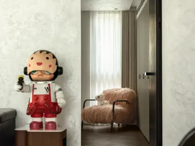 A small living area with a doll on a chair, a teddy bear on the floor, and a couch in the background, creating a cozy and inviting atmosphere