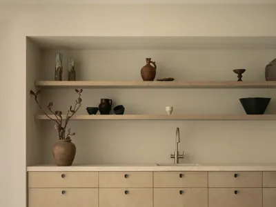 Modern kitchen with white walls, wooden floors, and decorative vases, featuring a sink and wooden cabinets