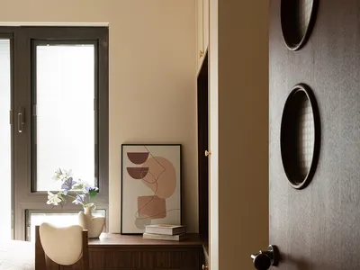 A calm bedroom with a white bed, two chairs, a desk, and a book, with a window nearby